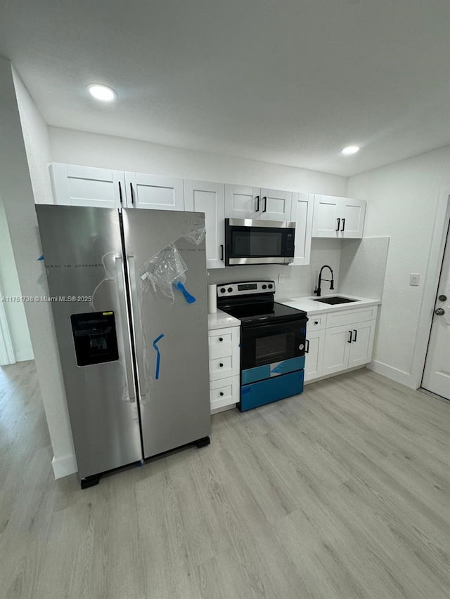 kitchen featuring light countertops, light wood-style flooring, appliances with stainless steel finishes, white cabinetry, and a sink