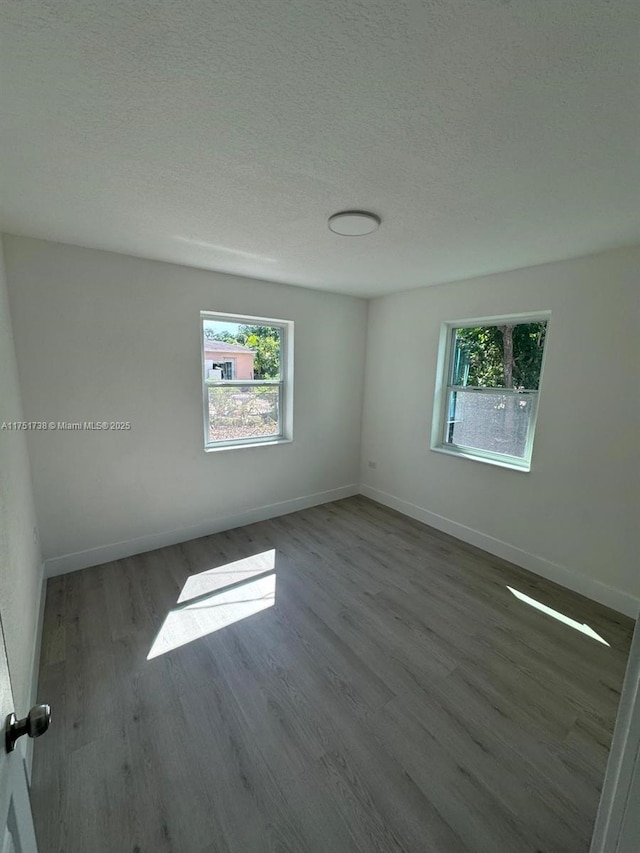 empty room with baseboards, a textured ceiling, and wood finished floors