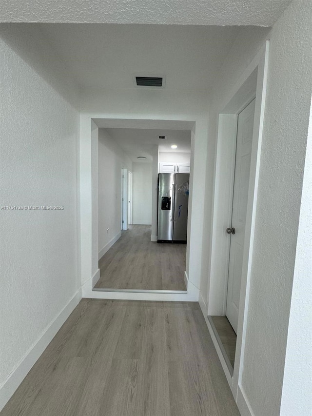 corridor with light wood finished floors, baseboards, visible vents, and a textured wall