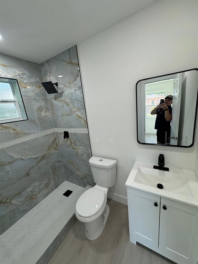 full bath with vanity, toilet, baseboards, tiled shower, and wood finished floors