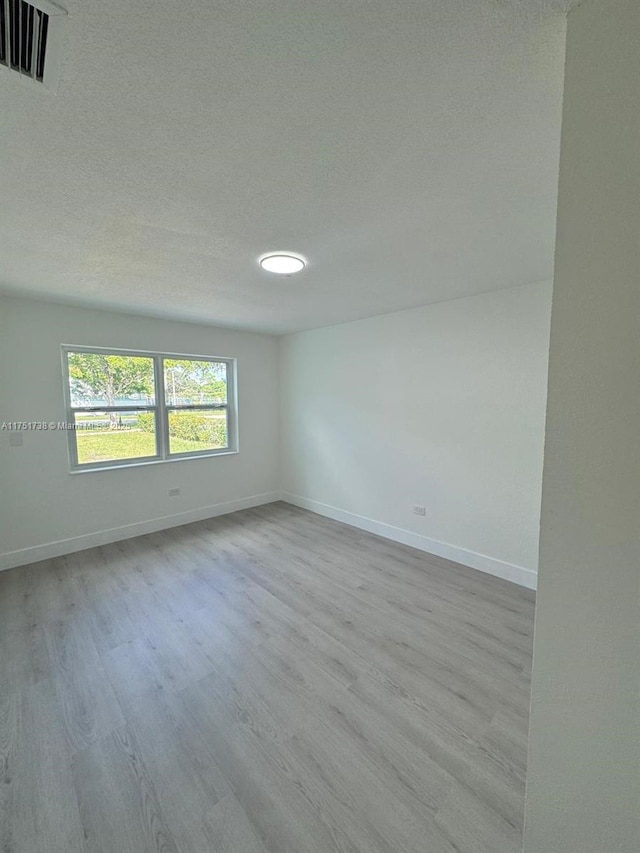 empty room with baseboards, visible vents, wood finished floors, and a textured ceiling