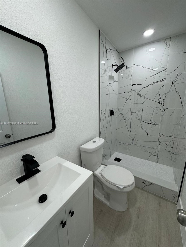 bathroom with a marble finish shower, toilet, wood finished floors, vanity, and a textured wall