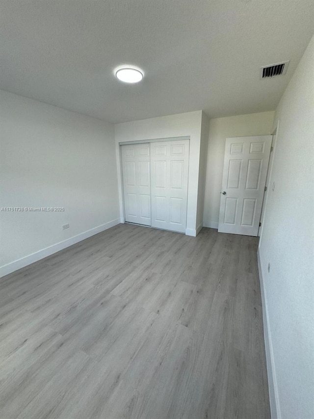 unfurnished bedroom featuring wood finished floors, a closet, baseboards, and visible vents