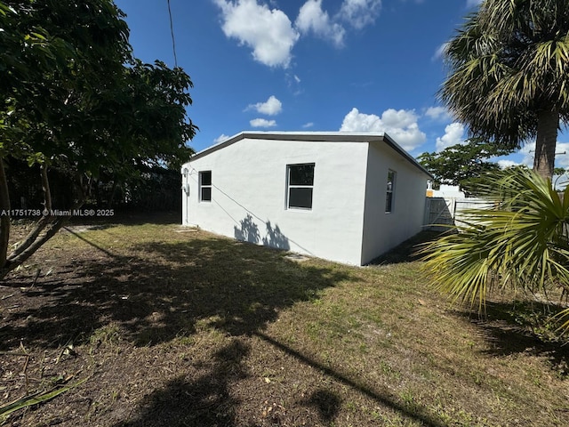 view of side of home featuring stucco siding, fence, and a lawn