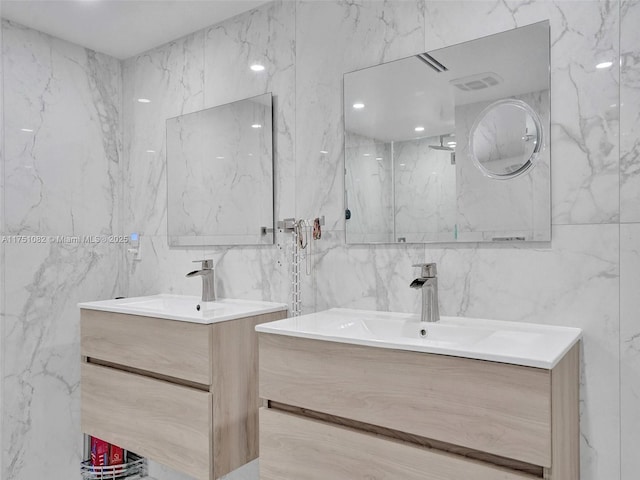 full bath featuring two vanities, a sink, tile walls, and stone wall