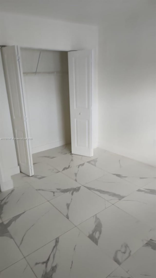 unfurnished bedroom with a closet, marble finish floor, and baseboards