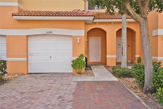 entrance to property with a tile roof, decorative driveway, a garage, and stucco siding