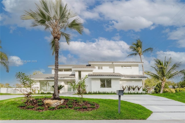 view of front facade with a front yard, a tile roof, curved driveway, and stucco siding