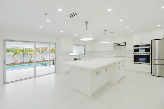 kitchen with light countertops, hanging light fixtures, appliances with stainless steel finishes, white cabinetry, and a kitchen island