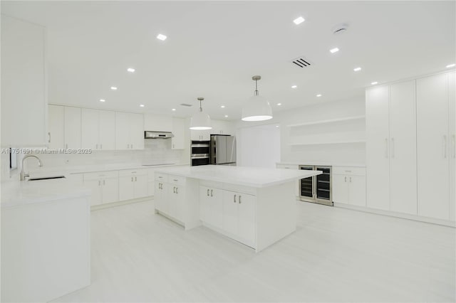 kitchen with pendant lighting, a large island, appliances with stainless steel finishes, white cabinetry, and a sink