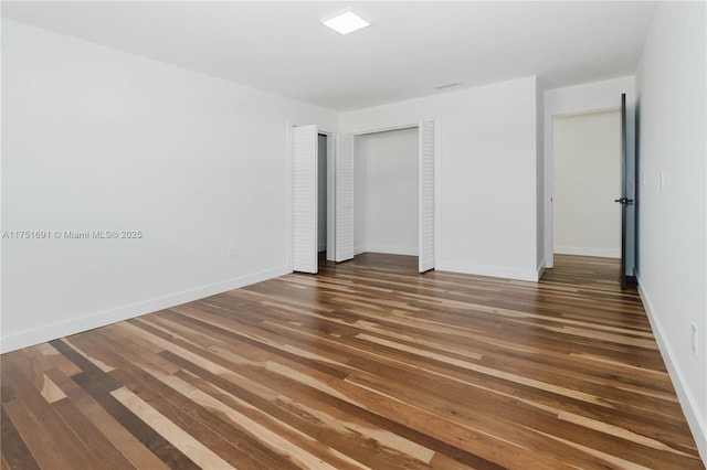 unfurnished bedroom with baseboards and dark wood-type flooring