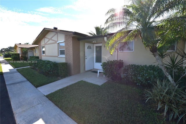 view of front facade with brick siding, a front lawn, and stucco siding