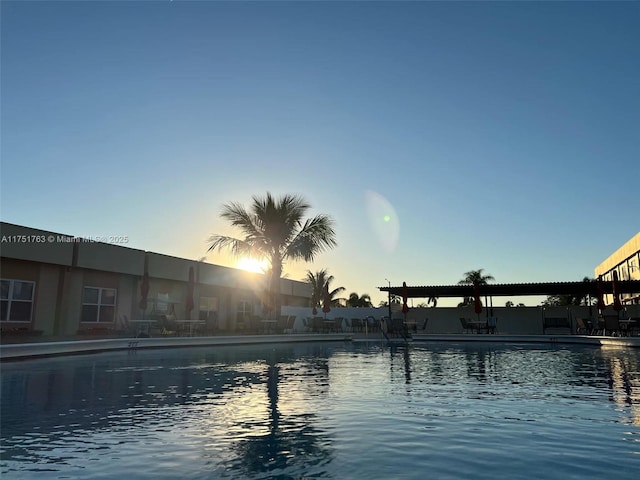 pool at dusk featuring a water view and a community pool