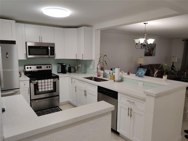 kitchen featuring stainless steel appliances, a peninsula, a sink, white cabinets, and decorative light fixtures