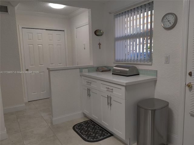 kitchen with light tile patterned floors, visible vents, white cabinets, light countertops, and crown molding