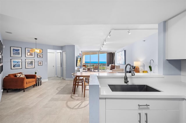 kitchen featuring rail lighting, a peninsula, light countertops, a sink, and open floor plan