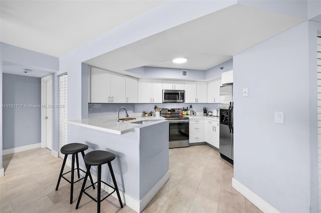 kitchen featuring a peninsula, white cabinets, a breakfast bar, stainless steel appliances, and baseboards
