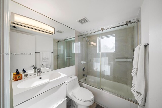 full bathroom with visible vents, toilet, vanity, and shower / bath combination with glass door