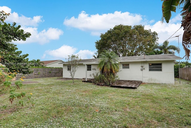 rear view of house featuring a lawn, fence, and stucco siding