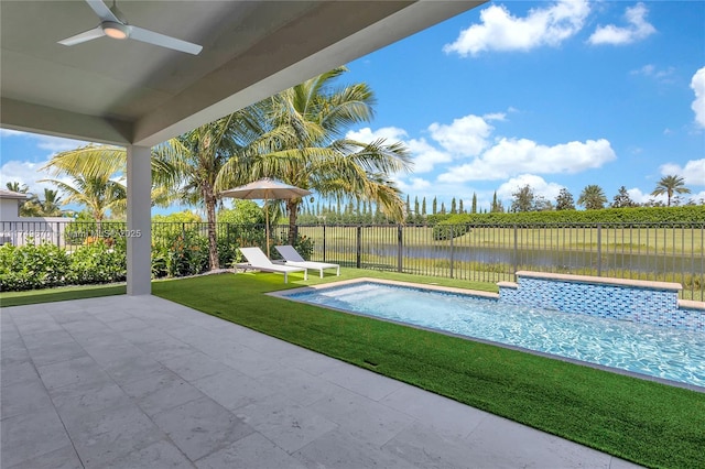 view of swimming pool featuring a lawn, a ceiling fan, a fenced backyard, a water view, and a patio area