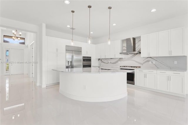 kitchen featuring a center island with sink, stainless steel appliances, white cabinetry, a sink, and wall chimney range hood