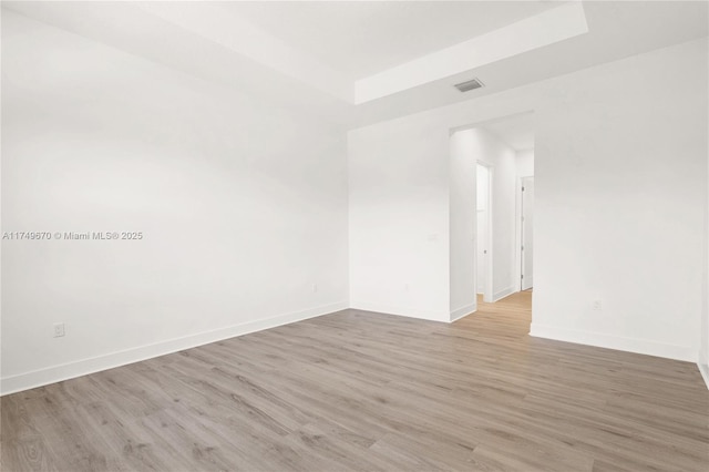 empty room with a raised ceiling, visible vents, light wood-style flooring, and baseboards