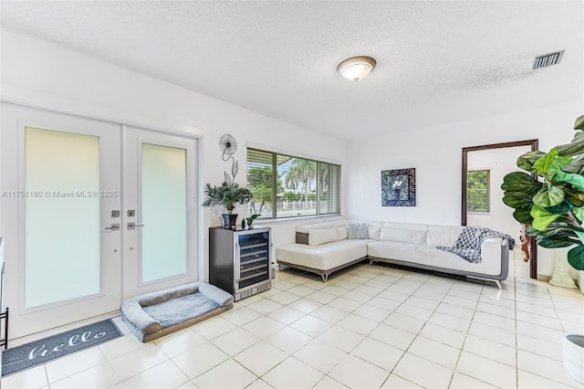 unfurnished living room with a textured ceiling, light tile patterned floors, wine cooler, visible vents, and french doors