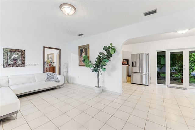 unfurnished living room featuring visible vents, arched walkways, a textured ceiling, and light tile patterned flooring