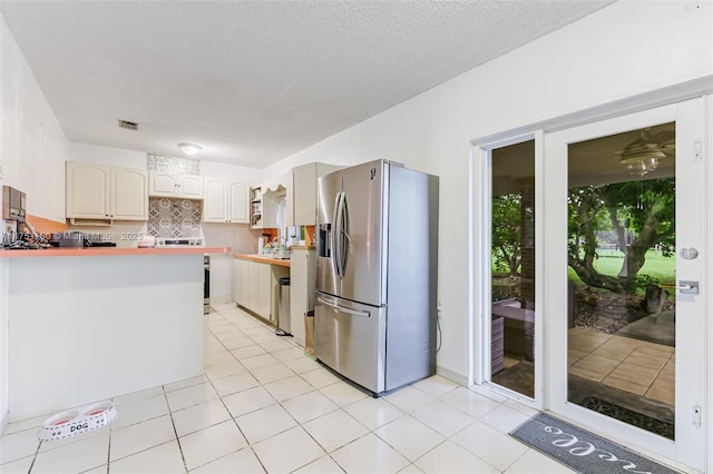 kitchen with light tile patterned floors, decorative backsplash, a peninsula, a textured ceiling, and stainless steel refrigerator with ice dispenser