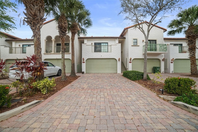 mediterranean / spanish home featuring an attached garage, a balcony, decorative driveway, and stucco siding