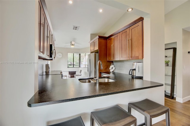 kitchen with visible vents, dark countertops, brown cabinets, a peninsula, and a sink