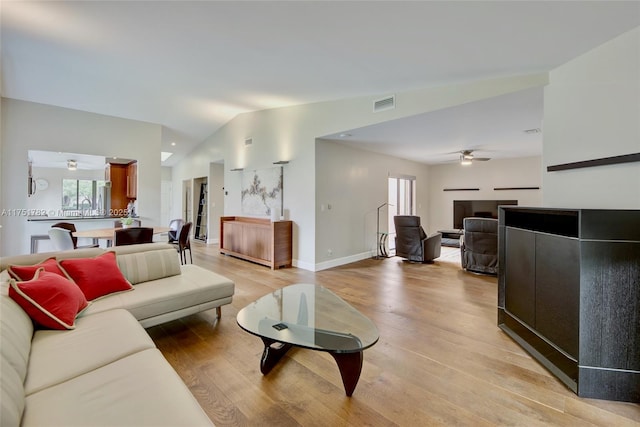 living room featuring a ceiling fan, baseboards, vaulted ceiling, visible vents, and light wood-style floors