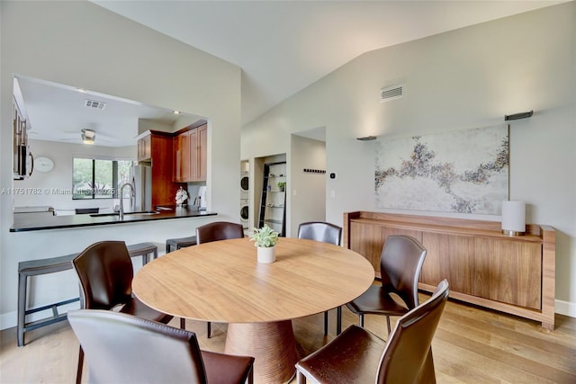 dining area featuring lofted ceiling, light wood-style floors, visible vents, and stacked washer and clothes dryer