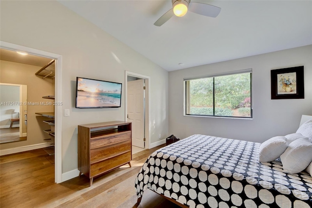 bedroom featuring lofted ceiling, light wood-style floors, a spacious closet, and baseboards