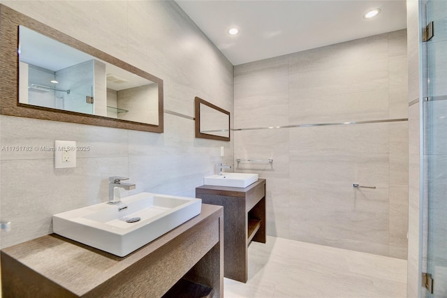 bathroom featuring a stall shower, tile walls, two vanities, and a sink