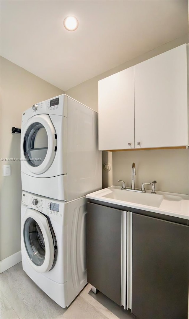 washroom featuring stacked washing maching and dryer, a sink, cabinet space, and baseboards