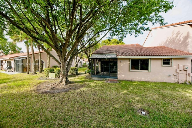 back of house featuring a sunroom, a tile roof, stucco siding, and a yard