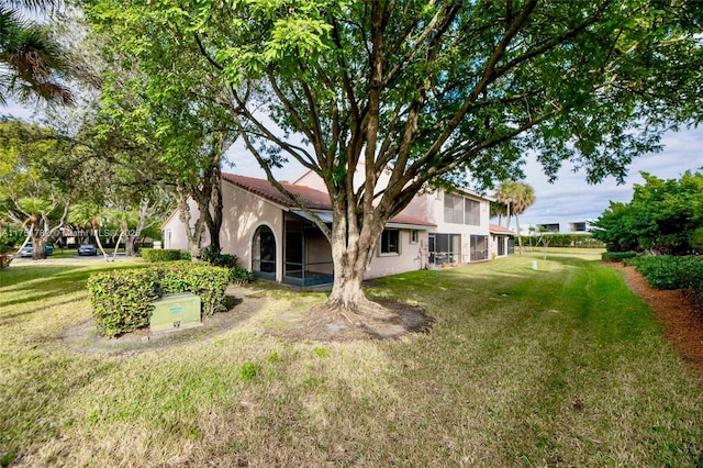 rear view of house with a lawn, a sunroom, and stucco siding