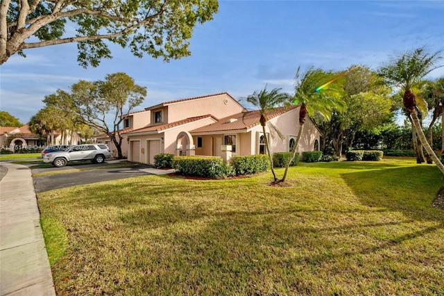 mediterranean / spanish-style home with a garage, driveway, a tiled roof, stucco siding, and a front yard