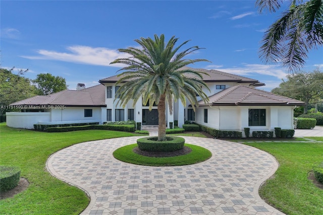 view of front of house with a tiled roof, a front lawn, curved driveway, and stucco siding