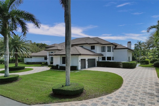 view of front of home featuring a garage, a chimney, decorative driveway, a front lawn, and stucco siding