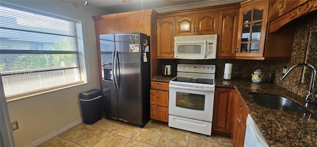 kitchen featuring white appliances, a sink, decorative backsplash, dark stone counters, and glass insert cabinets