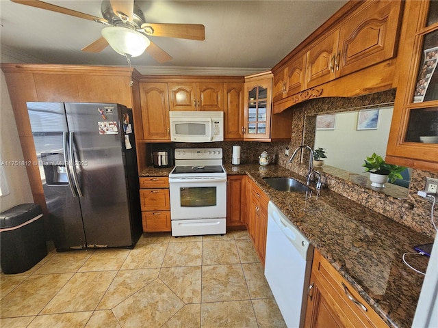 kitchen featuring white appliances, dark stone counters, glass insert cabinets, brown cabinets, and a sink