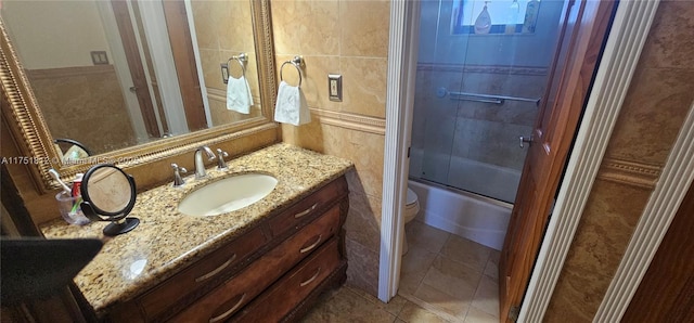 bathroom with shower / bath combination with glass door, tile walls, toilet, vanity, and tile patterned floors