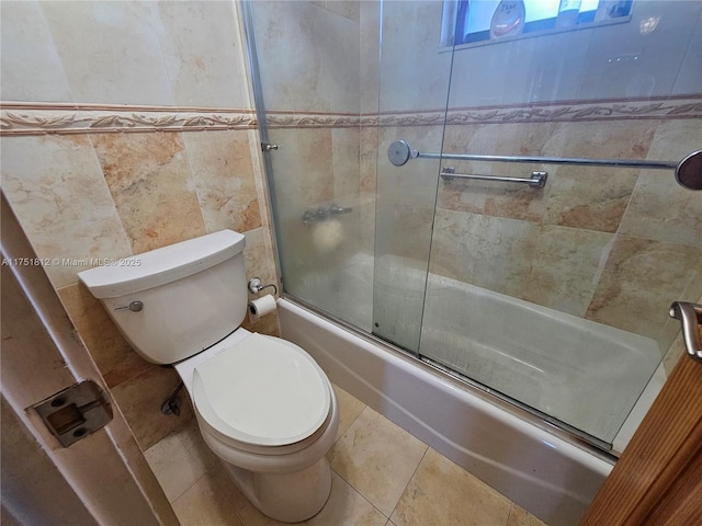 bathroom with toilet, tile patterned flooring, combined bath / shower with glass door, and tile walls