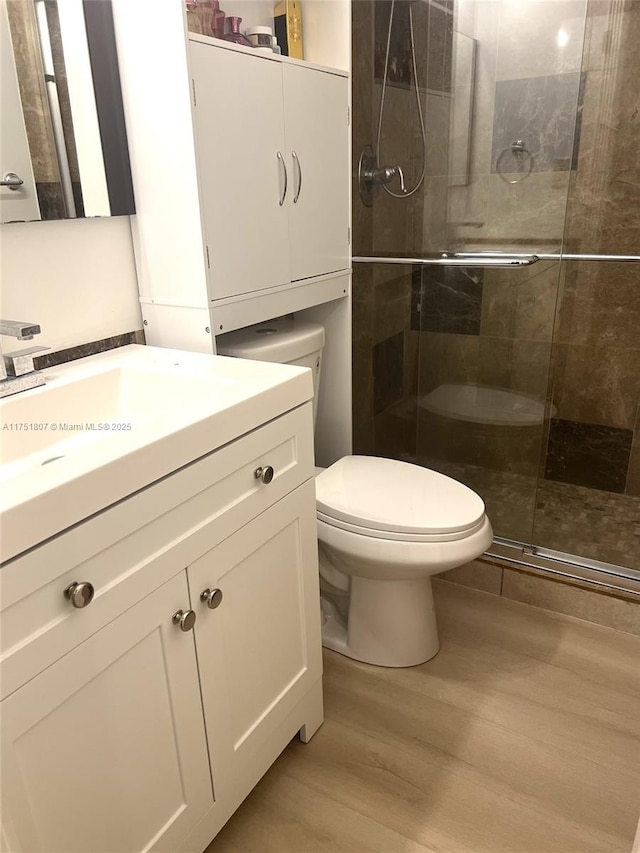 full bath with vanity, toilet, wood finished floors, and a stall shower