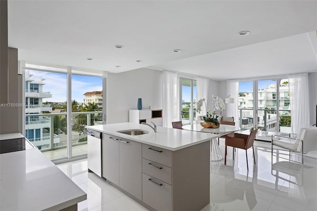 kitchen featuring expansive windows, a sink, light countertops, dishwasher, and a center island with sink