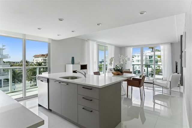 kitchen featuring gray cabinetry, a sink, light countertops, stainless steel dishwasher, and an island with sink