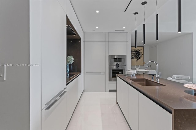 kitchen with modern cabinets, double oven, white cabinetry, pendant lighting, and a sink