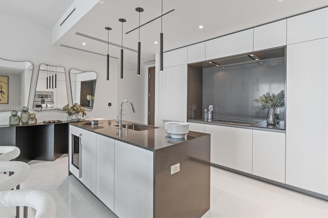 kitchen featuring a center island with sink, dark countertops, hanging light fixtures, white cabinetry, and modern cabinets